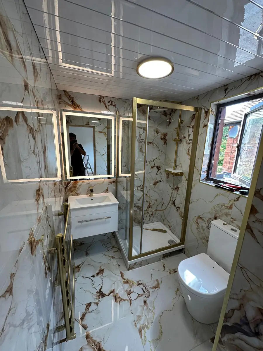 Completed bathroom renovation in Brent with white and gold marble-effect porcelain tiling, a gold-framed corner shower enclosure and a wall-hung vanity unit