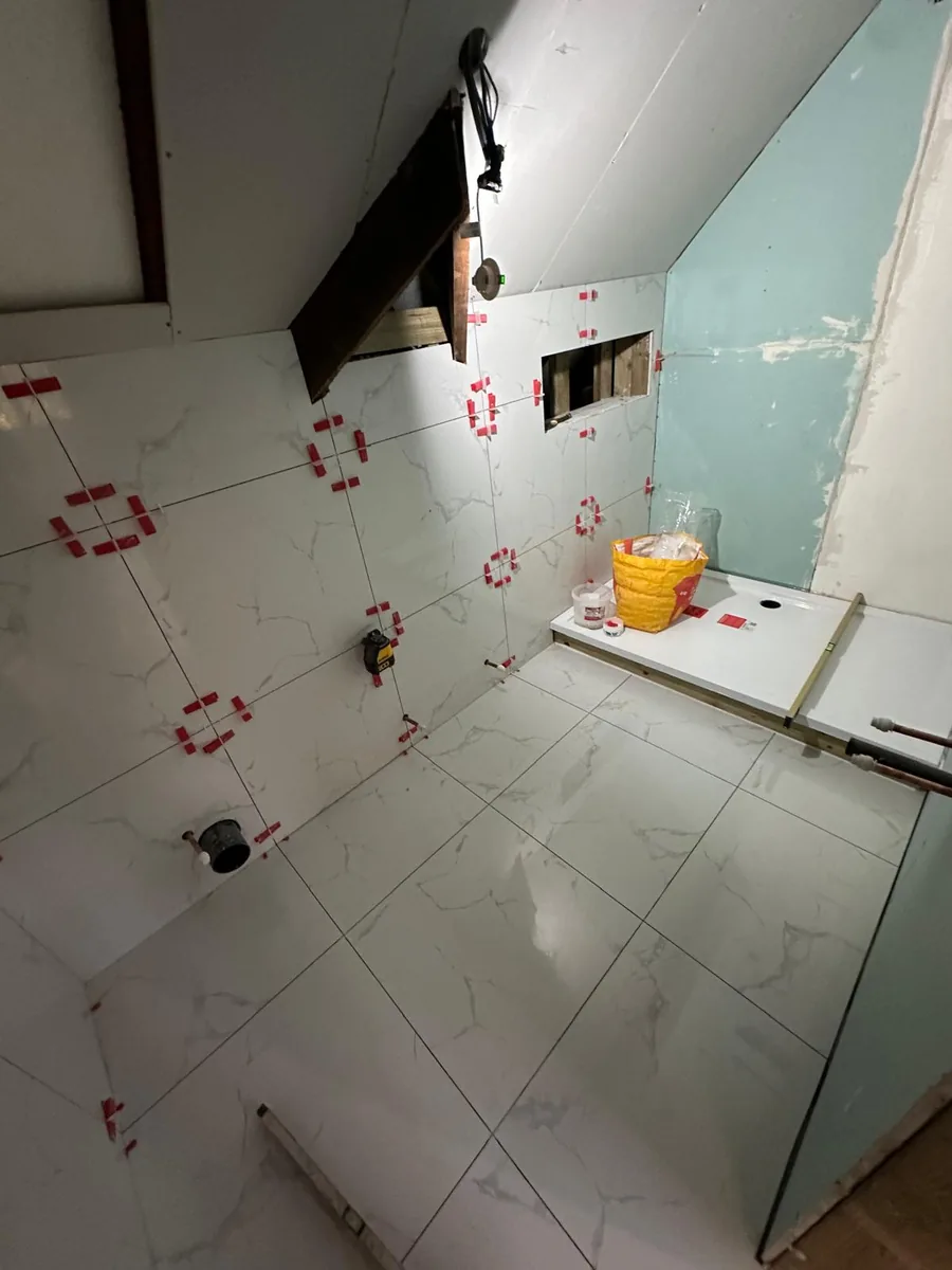 Marble-effect porcelain tiles being set on the walls and floor of the Croydon loft bathroom, with levelling clips still in place