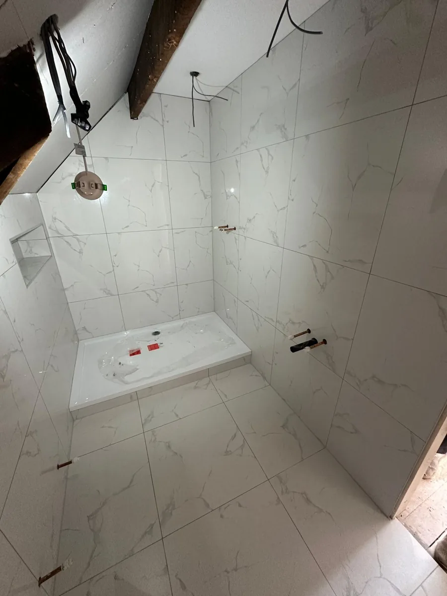 Tiled Croydon loft shower room with the low-profile shower tray fitted and shower and basin pipework stubbed out of the wall