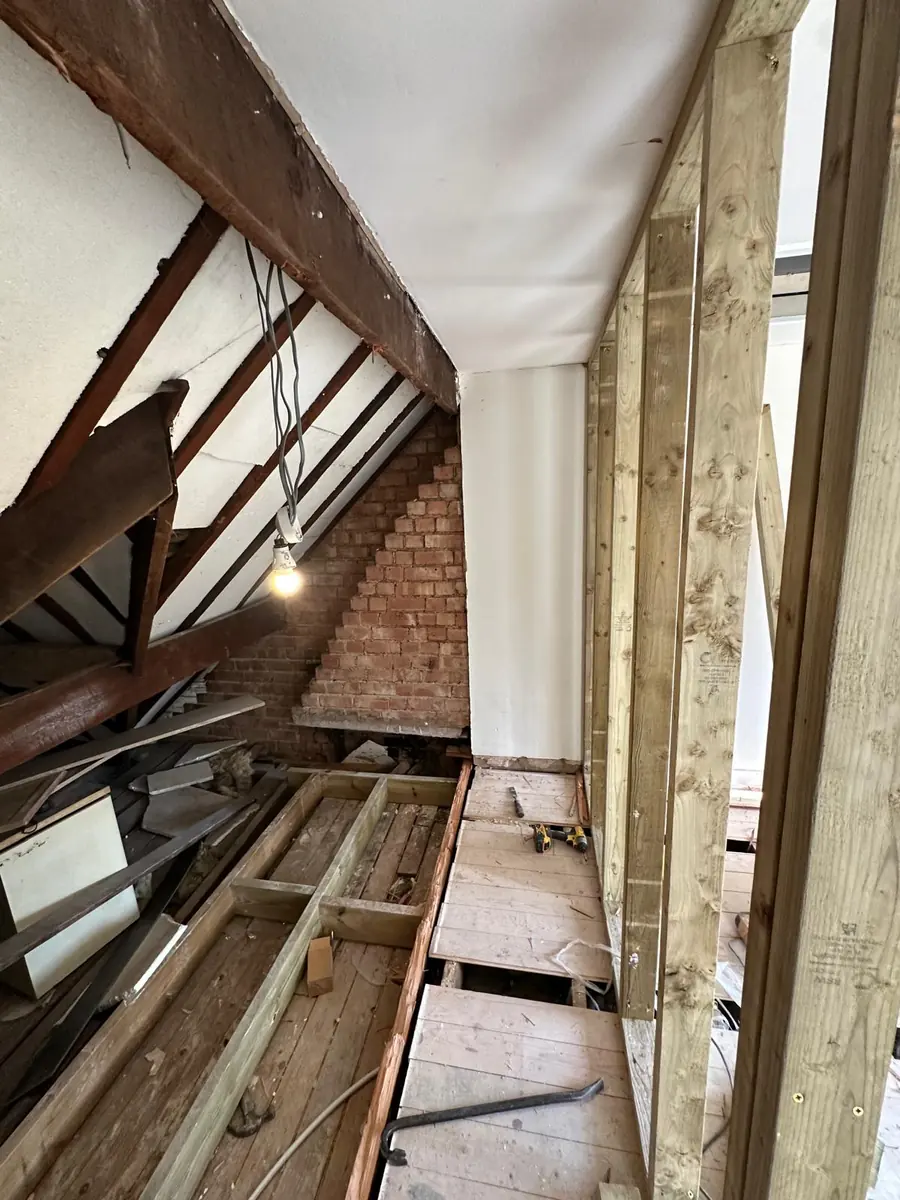 Croydon loft mid strip-out, with the old chimney breast exposed, dark original rafters and new timber stud framing going up