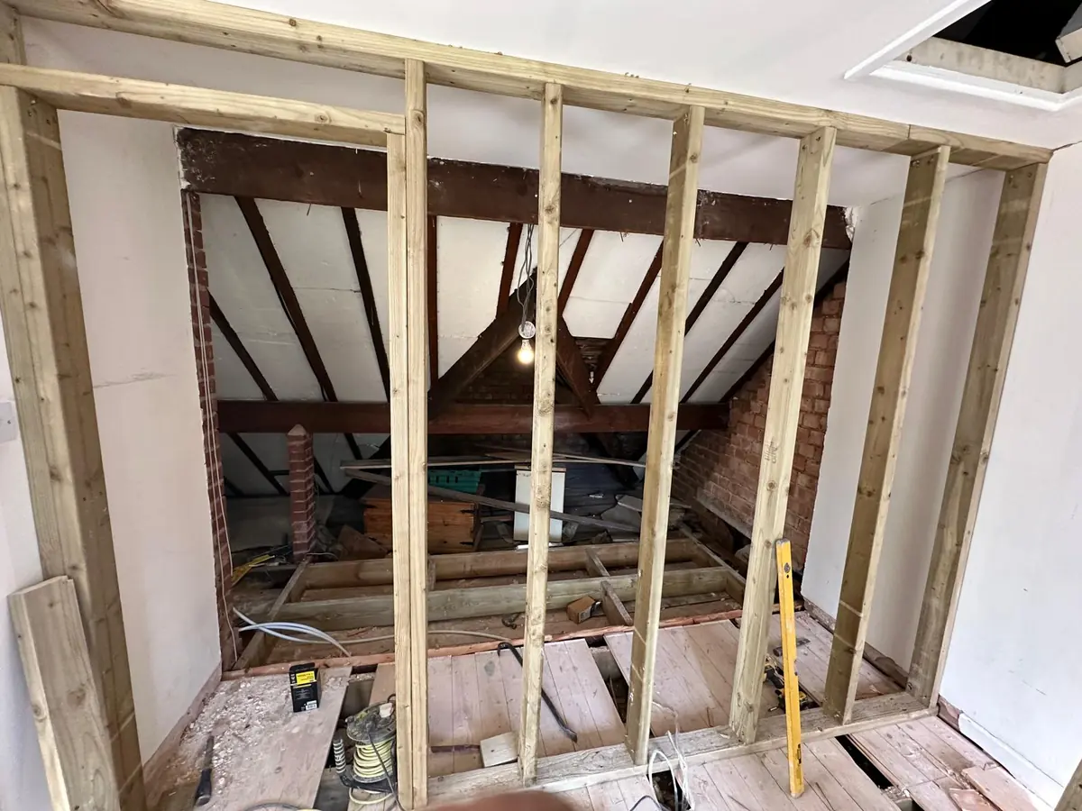 New timber stud partition framing built inside a Croydon loft, with floorboards lifted and roof structure still exposed behind