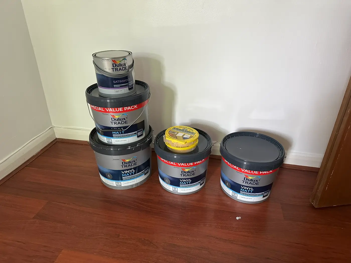 Tubs of trade vinyl matt emulsion and satinwood paint lined up on a wooden floor in a Brockley flat