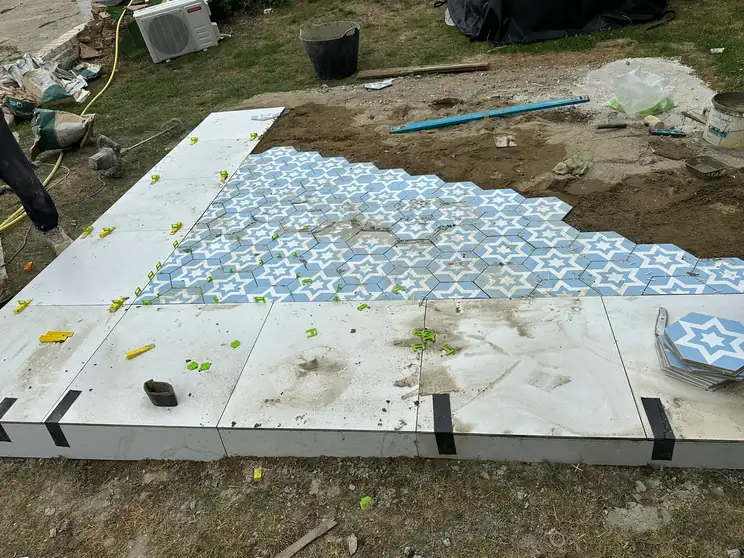 A patio being laid in large pale porcelain slabs with a blue and white patterned tile inset, levelling clips still in place