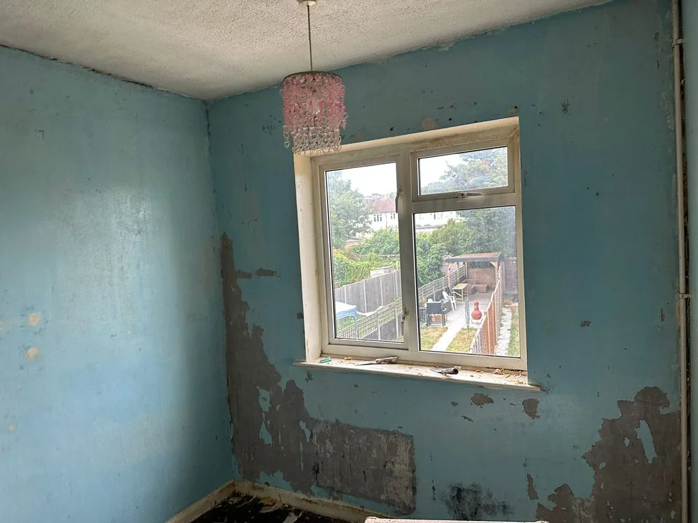 Bedroom mid-renovation with wallpaper stripped back to blown and damaged plaster beneath the window, Sidcup