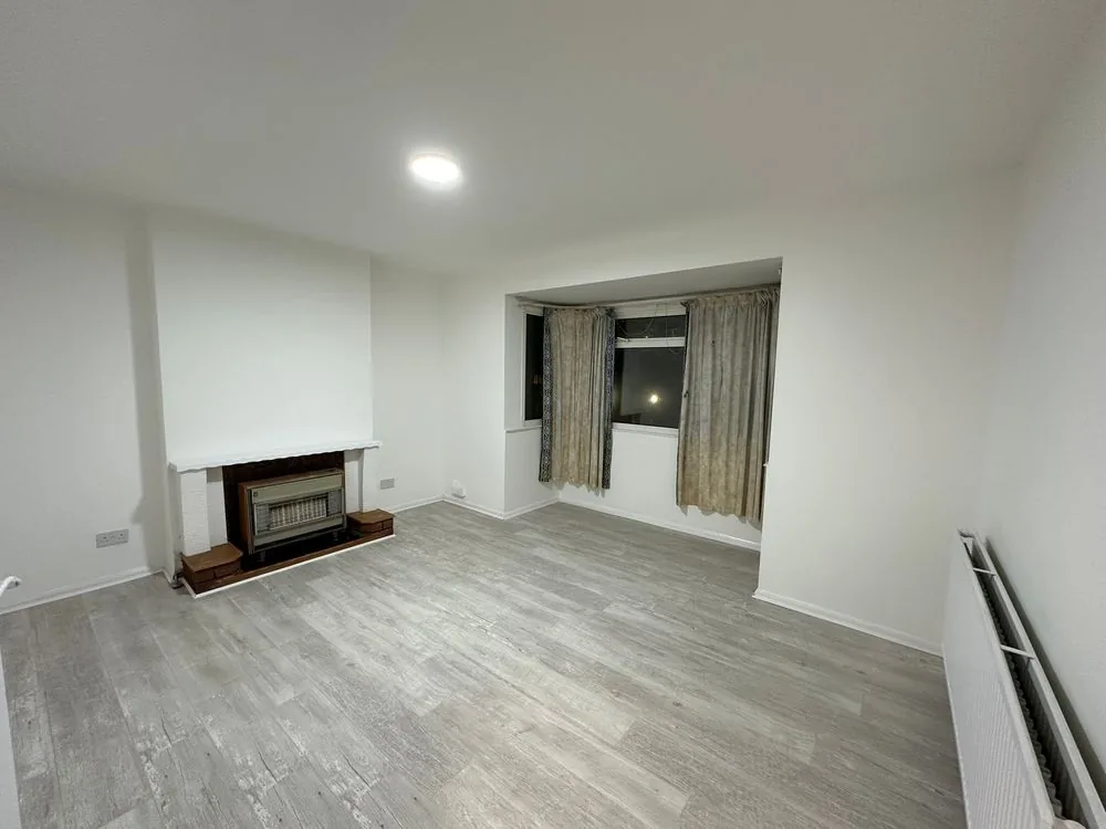 The same Sidcup living room after renovation, with freshly skimmed white walls, grey oak-effect flooring, LED ceiling lights and the gas fire retained