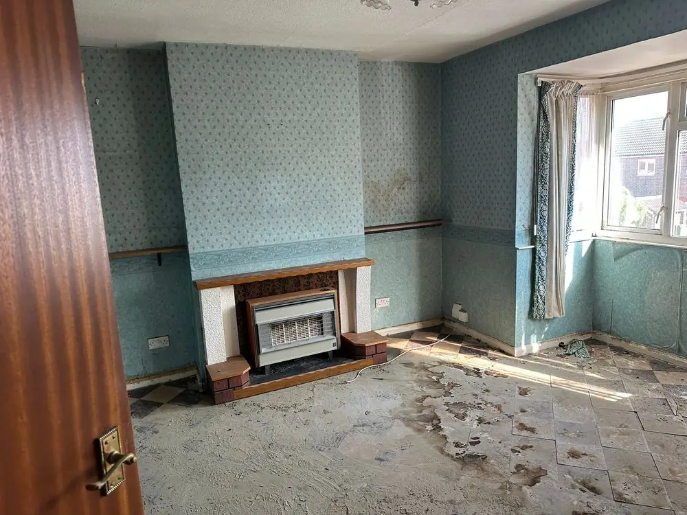 Living room before renovation in a Sidcup home, with patterned wallpaper, dado rails, a dated fire surround and lifted floor tiles