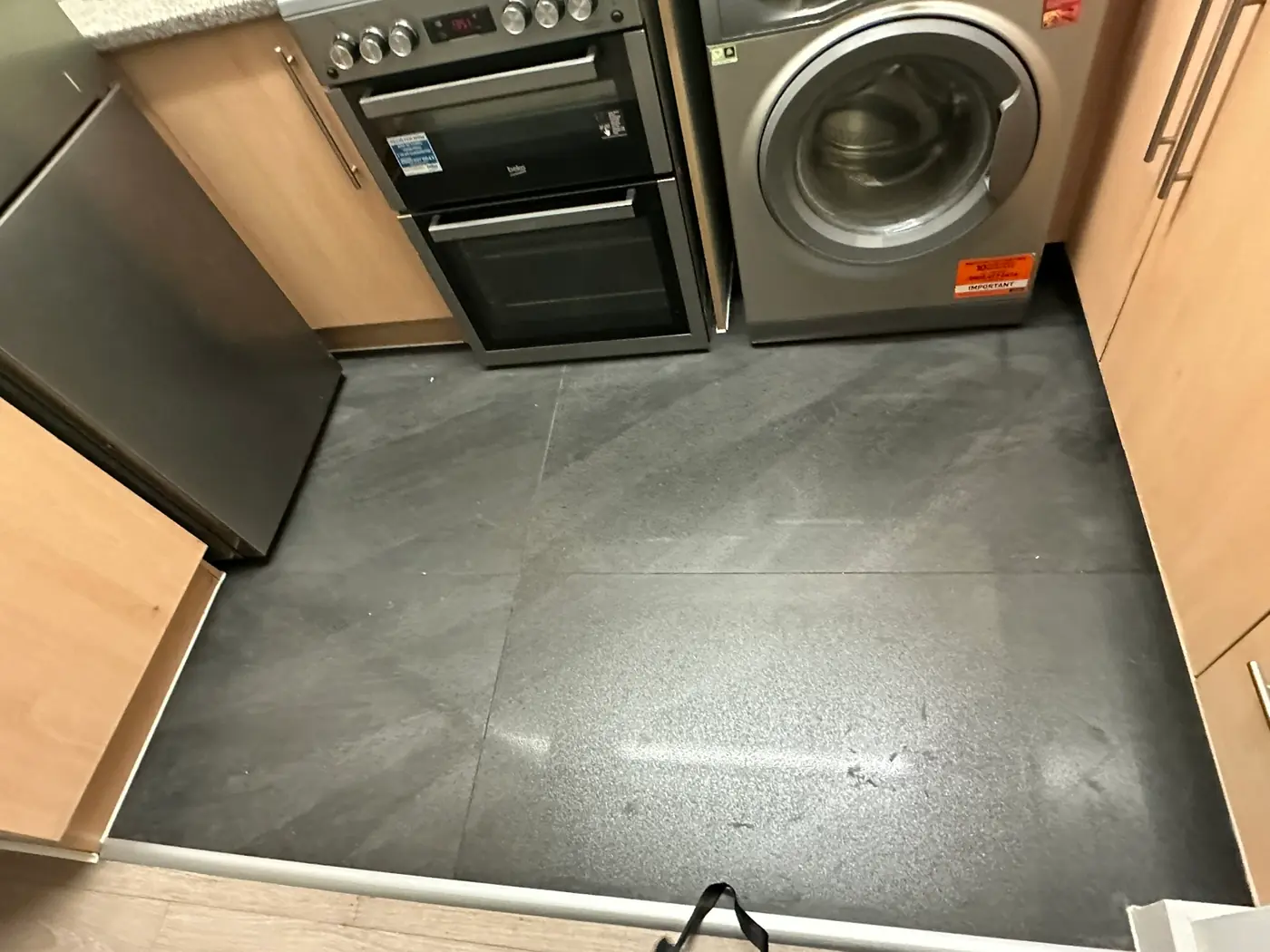 A kitchen floor relaid in large-format dark grey porcelain tiles between the units, in a Pimlico flat