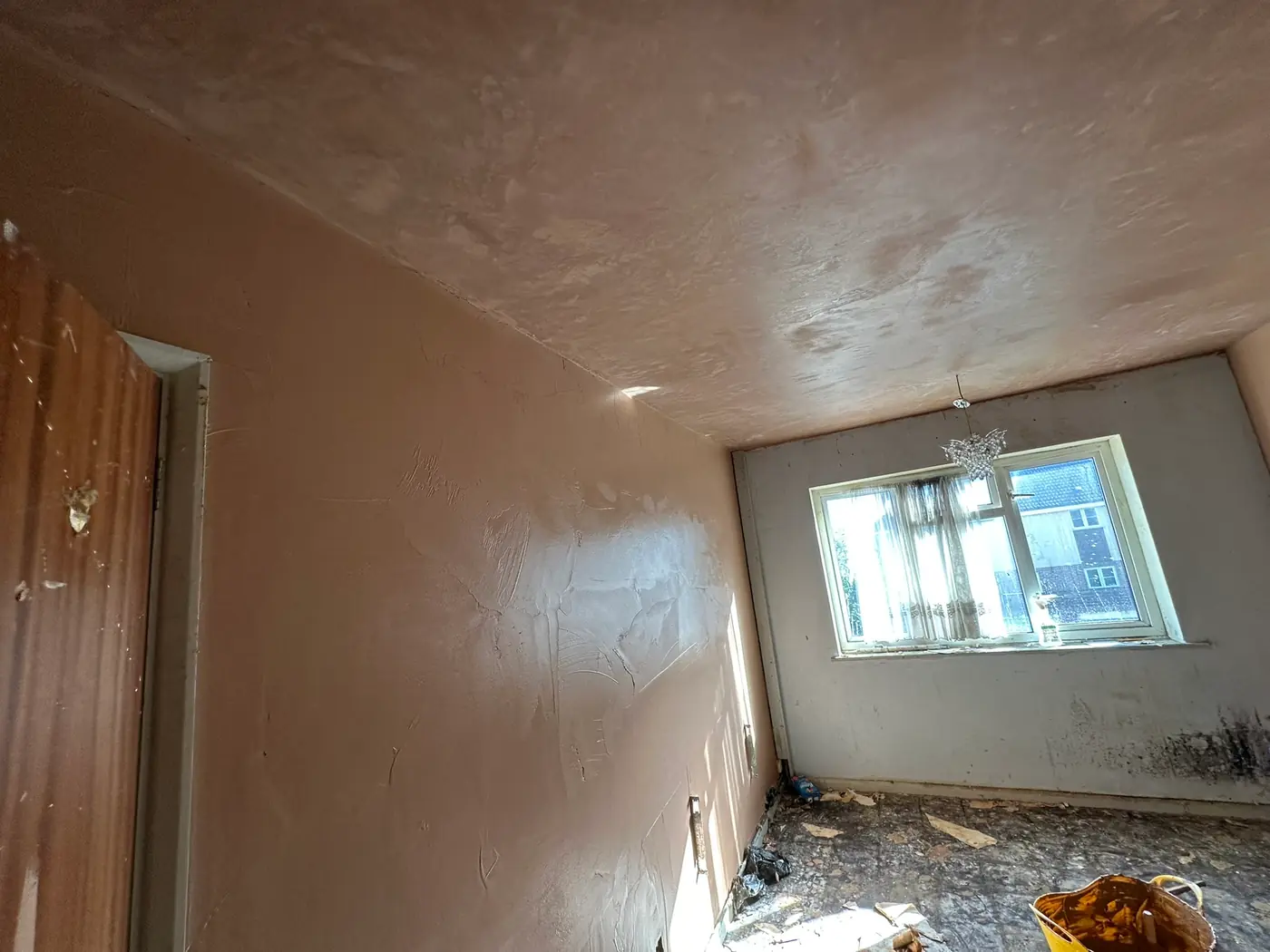 Bedroom walls and ceiling freshly skimmed in pink finishing plaster, still drying, in a Sidcup house