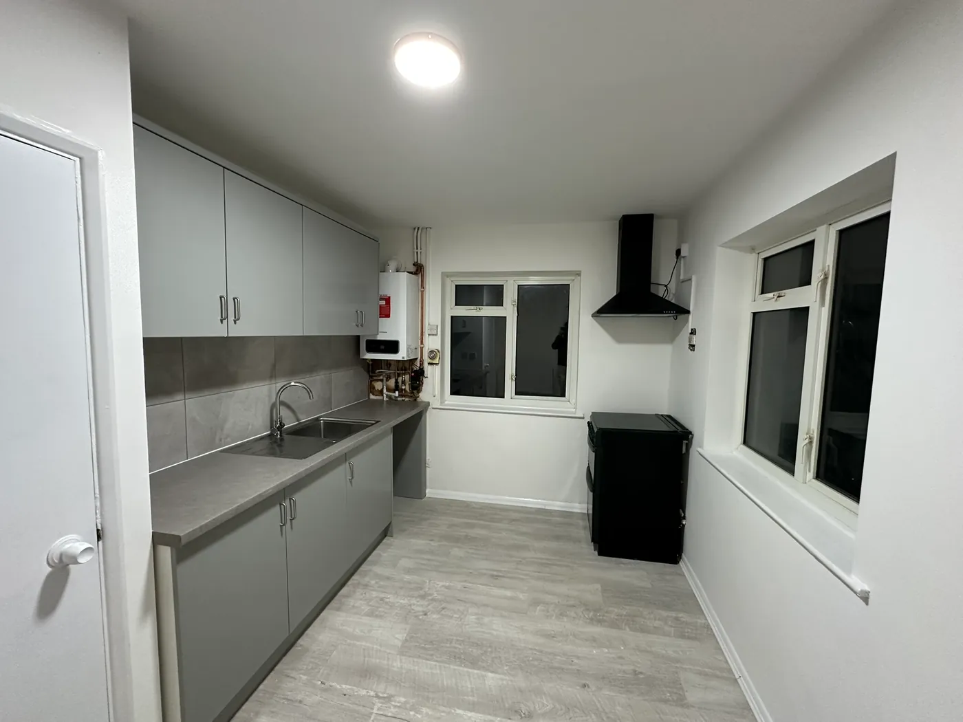 A finished galley kitchen in grey with a new wall-hung boiler at the far end, in a Sidcup house