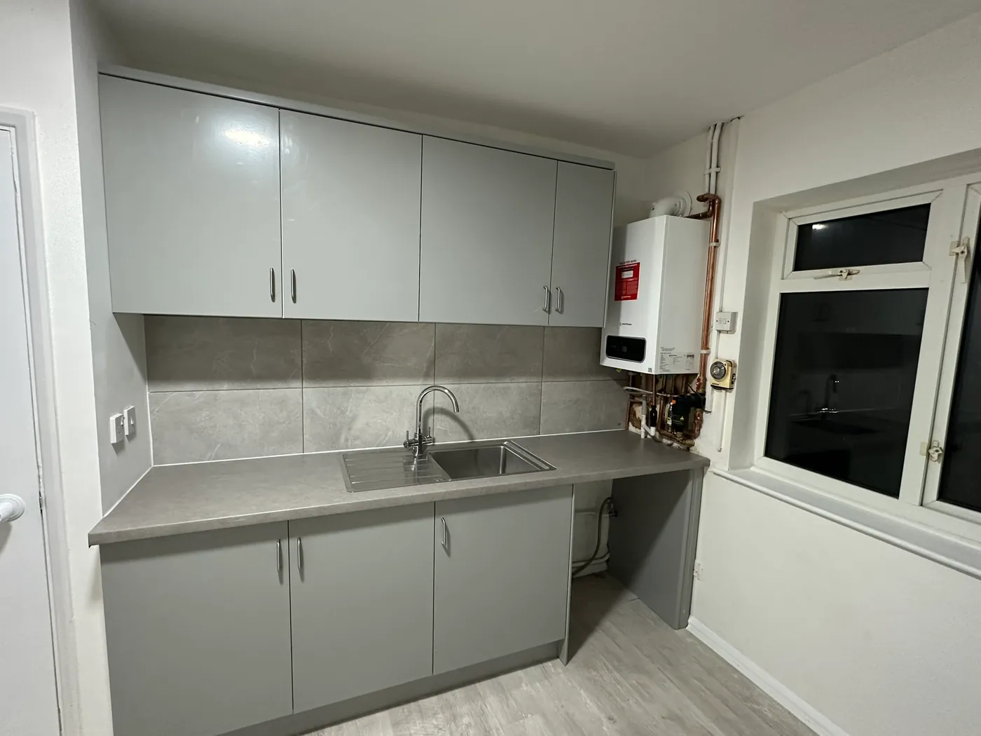 A new white wall-hung gas boiler with copper pipework beside new grey kitchen units in a Sidcup house
