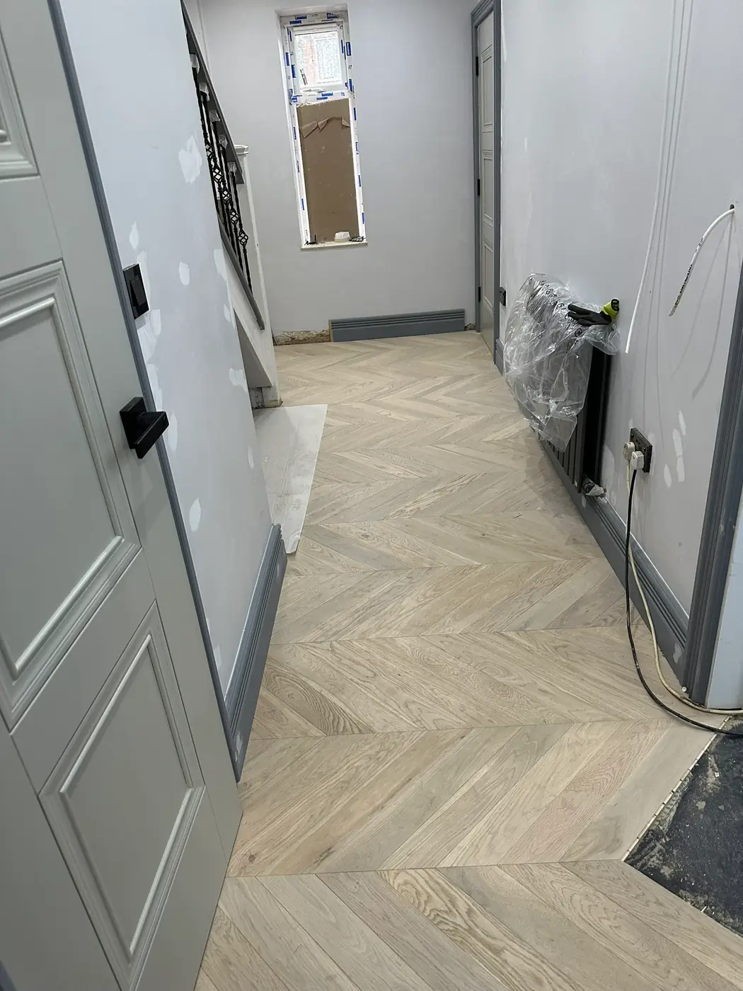 Light oak-effect chevron flooring being laid along a hallway, with skirting boards going in, in a Watford house