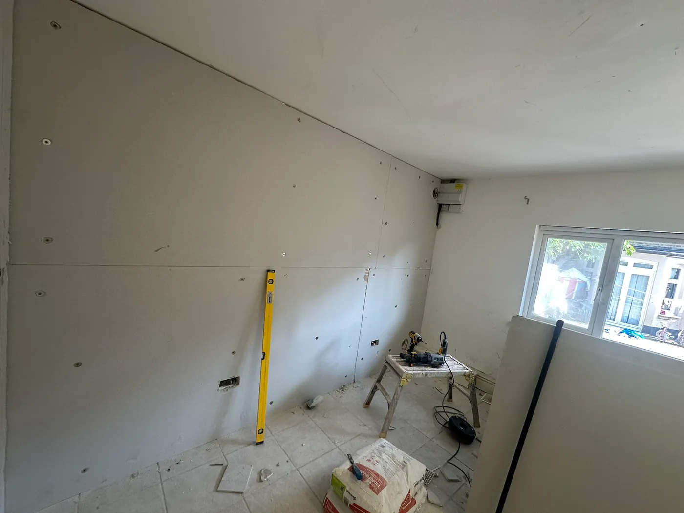 Plasterboard screwed over insulation boards on a room wall, with a spirit level and tools, in a Wembley house
